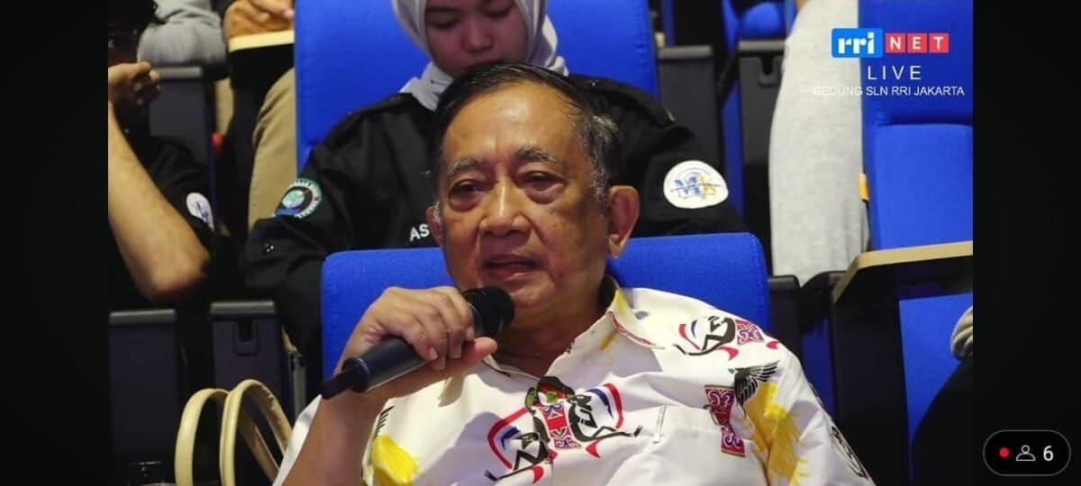 Berkas foto pria berbicara dengan mikrofon di acara resmi di dalam ruangan.