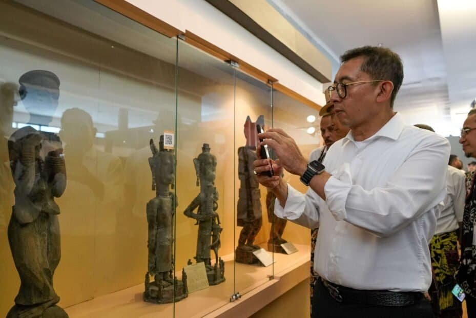 Alternatif teks: Koleksi patung kuno di museum oleh pengunjung pria berpakaian putih.